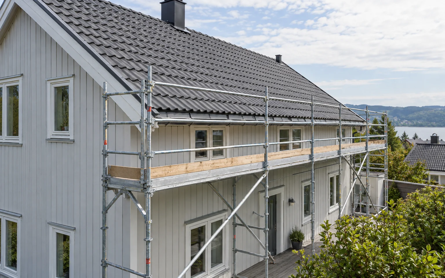 Stillas med rekkverk langs takfoten på et trehus.